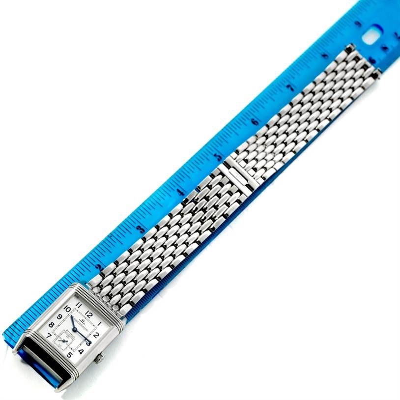 The image displays a Jaeger LeCoultre Reverso 270.8.62 Men's Stainless Steel Silver Dial 270.8.62 Men's Stainless Steel Silver Dial watch laying flat next to a ruler, highlighting its face and metal bracelet.