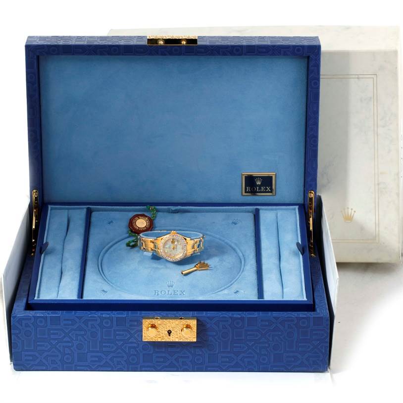 The Rolex Pearlmaster 69298 Women's Yellow Gold Mother of Pearl Dial 69298 Women's Yellow Gold Mother of Pearl Dial watch is displayed inside an open blue box with accessories, including a seal and a key.