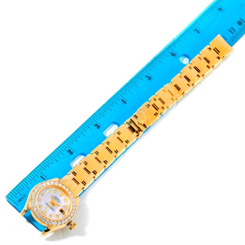 The image shows a Rolex Pearlmaster 69298 Women's Yellow Gold Mother of Pearl Dial 69298 Women's Yellow Gold Mother of Pearl Dial watch laid out flat next to a blue ruler, showcasing its face and band.