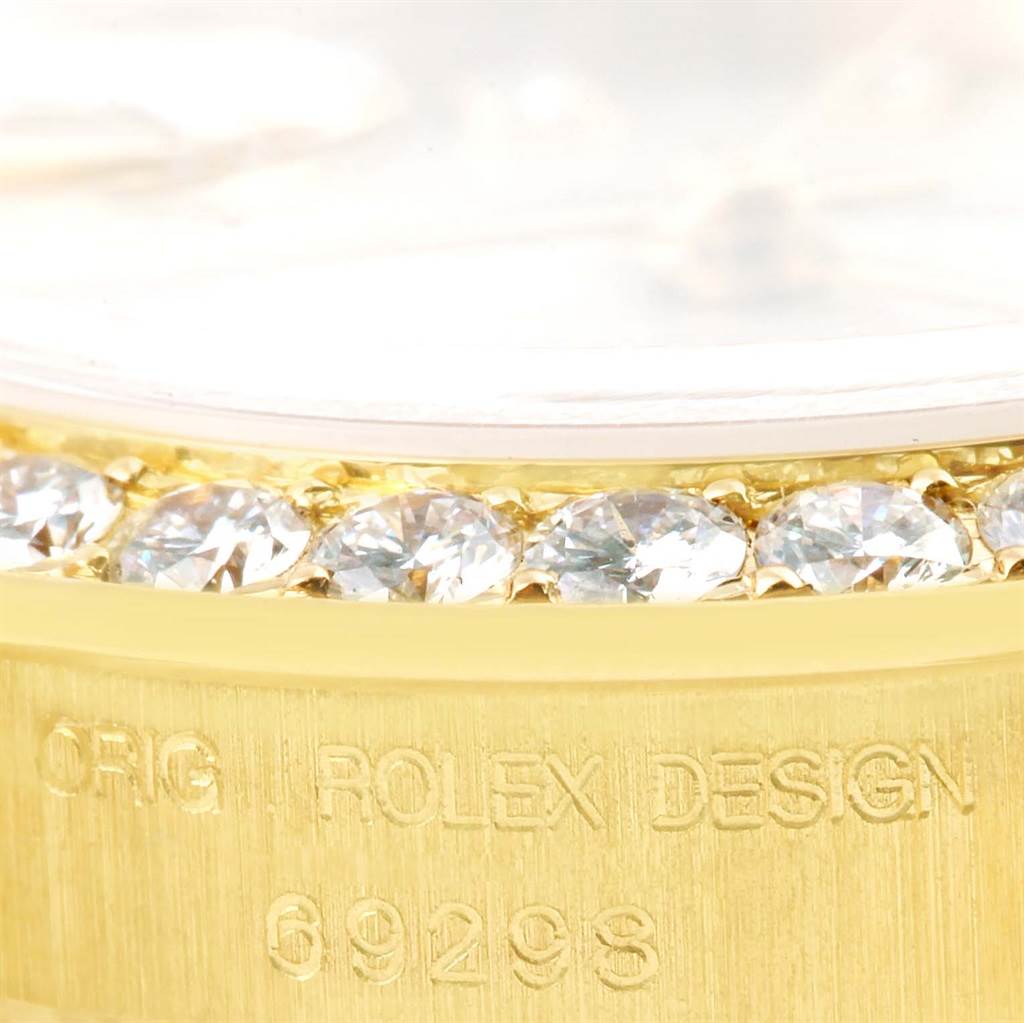 The image shows a close-up of the bezel adorned with diamonds and part of the engraved case of a Rolex Pearlmaster 69298 Women's Yellow Gold Silver Dial 69298 Women's Yellow Gold Silver Dial watch.