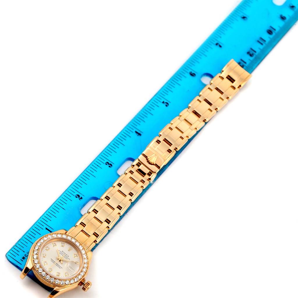 The image shows a Rolex Pearlmaster 69298 Women's Yellow Gold Silver Dial 69298 Women's Yellow Gold Silver Dial watch, lying flat with its band extended alongside a blue ruler.