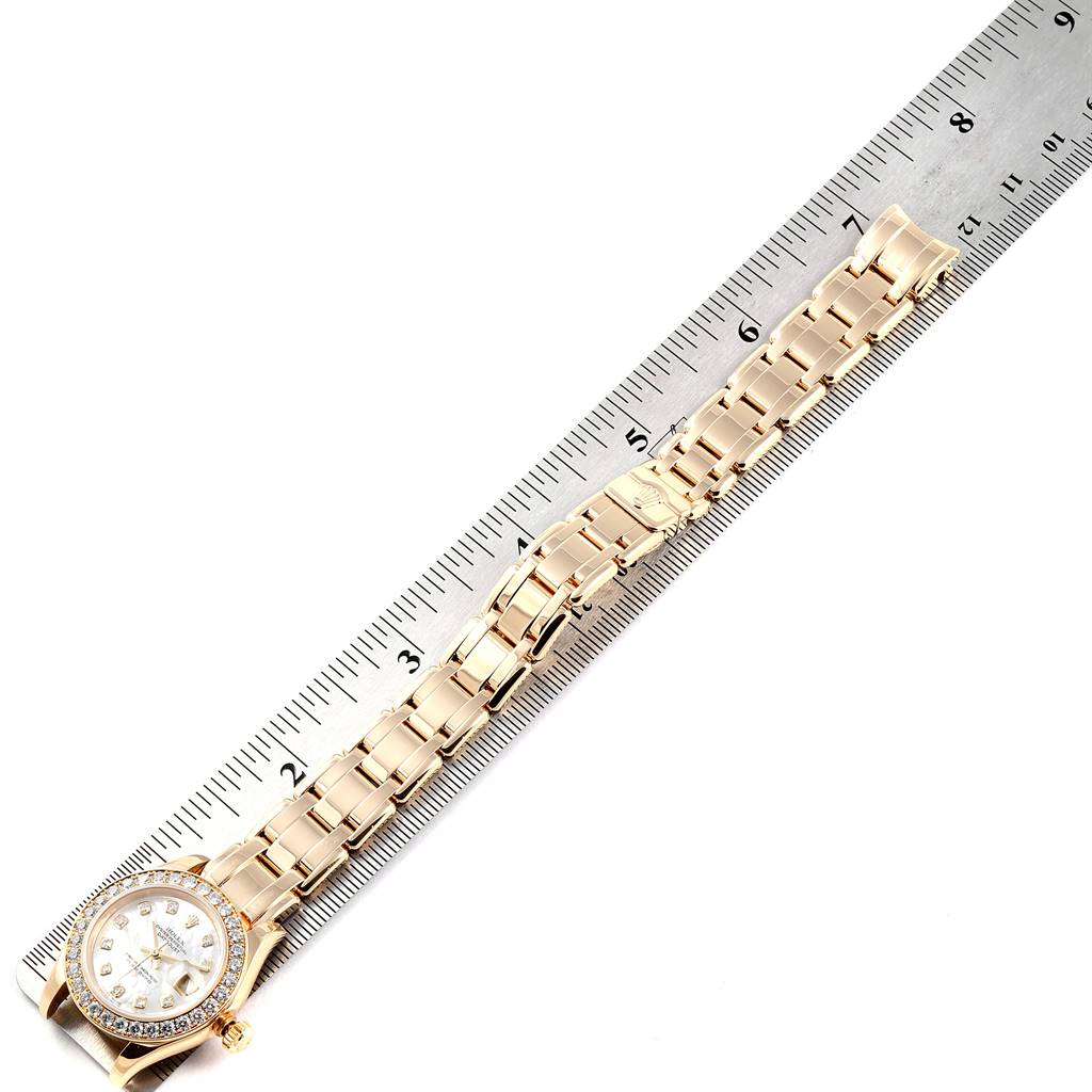 The image shows a Rolex Pearlmaster 80298 Women's Yellow Gold Mother of Pearl Dial 80298 Women's Yellow Gold Mother of Pearl Dial watch laying flat next to a ruler, highlighting its band and face.