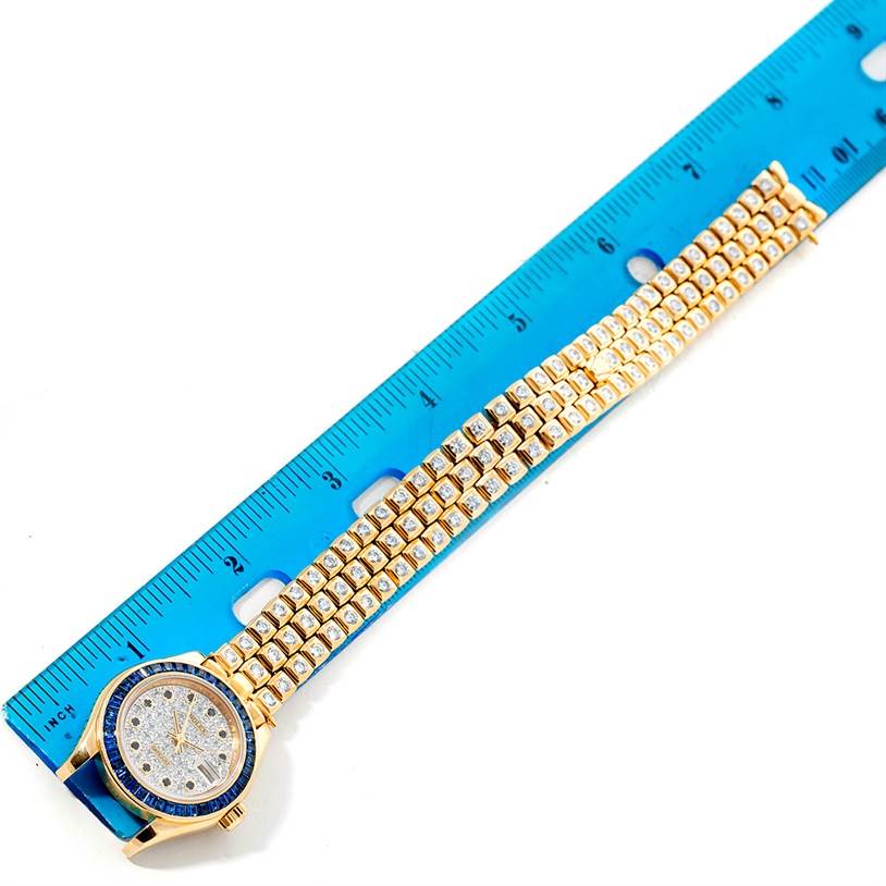 The image shows a top view of a Rolex Pearlmaster 69308 Women's Yellow Gold  69308 Women's Yellow Gold  watch next to a ruler, highlighting the entire bracelet and dial.